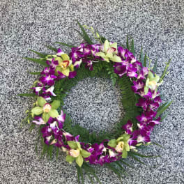 Circular orchid wreath with purple and green blooms on a stone surface