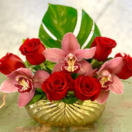 Red roses and pink orchids arranged in a gold vase