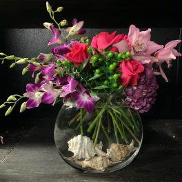 Bouquet of pink roses and purple orchids in a glass bowl vase