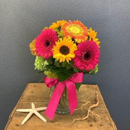 Bright gerbera daisy bouquet in a glass vase with a pink ribbon