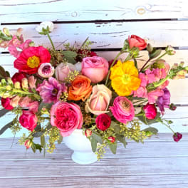 Colorful arrangement of roses, ranunculus, poppies, and snapdragons in a white pedestal vase