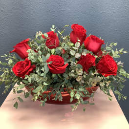 Red roses arranged in a low red container with eucalyptus foliage