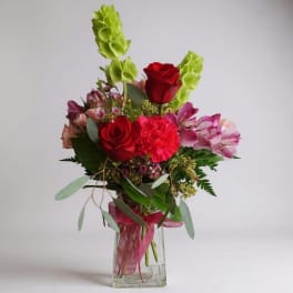 Red roses and pink flowers arranged in a clear glass vase.