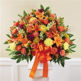 Orange and yellow mixed flower arrangement with a large ribbon in a white vase