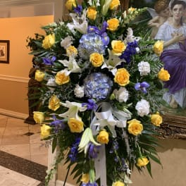 Large standing floral spray with yellow roses, white lilies, and purple blooms