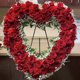 Heart-shaped red rose wreath on a stand with white filler flowers