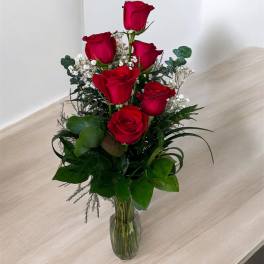 Red roses arranged in a clear glass vase with white filler flowers