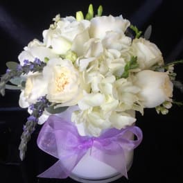 White floral bouquet in a white vase with a purple ribbon
