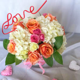 Bouquet of peach, pink, and white roses with a red wire "love" topper