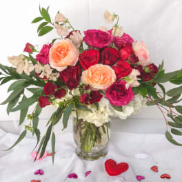 Mixed roses and sweet pea in a clear glass vase with heart confetti