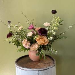 Mixed bouquet of roses, ranunculus, and carnations in a pink vase
