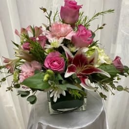 Pink roses and lilies arranged in a square glass vase
