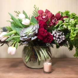 Mixed floral arrangement in a glass vase with a candle in front