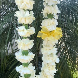 Two white flower leis with a yellow ribbon draped over palm fronds