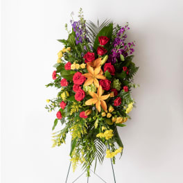 Tall standing spray with orange lilies, red roses, yellow blooms, and purple flowers on an easel.