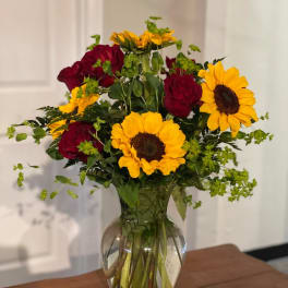 Red roses and yellow sunflowers arranged in a clear glass vase