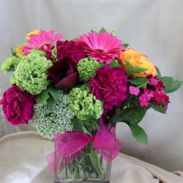 Bright mixed bouquet in a clear glass vase with a pink ribbon