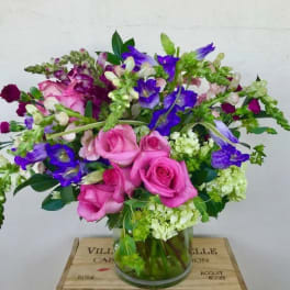 Pink roses and purple flowers arranged in a glass vase