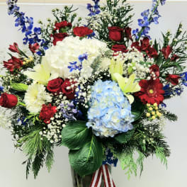 Large mixed floral arrangement in a clear vase with red, white, blue, and yellow blooms
