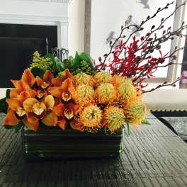 Orange orchids and yellow pincushion blooms in a rectangular vase