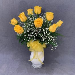 Yellow roses in a white vase with baby's breath and a yellow ribbon