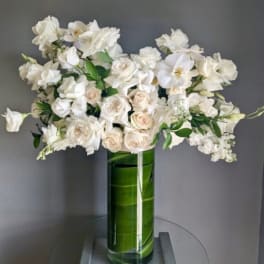 White roses and orchids arranged in a tall green glass vase
