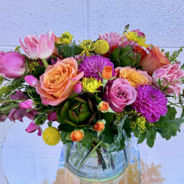 Mixed bouquet of pink, peach, and yellow flowers in a clear glass vase