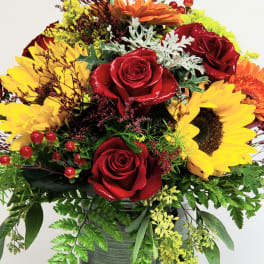 Red roses and yellow sunflowers in a dark vase with mixed greenery