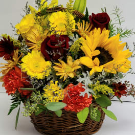 Basket arrangement of yellow sunflowers, red roses, and orange flowers