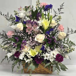 Basket arrangement of roses, lilies, carnations, and daisies in white, purple, and pink