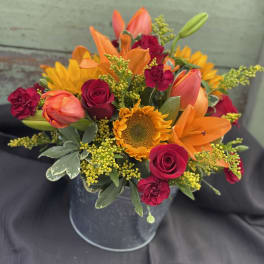 Bouquet of orange lilies, red roses, and a sunflower in a metal bucket
