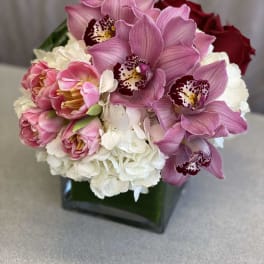 Pink orchids and roses arranged in a square glass vase