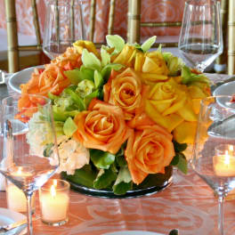 Orange and yellow rose centerpiece on a table with candles and wine glasses