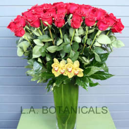Tall vase arrangement of red roses with yellow orchids