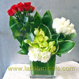 Red roses, white blooms, and green orchids in a square glass vase