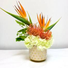 Tropical flower arrangement with orange bird of paradise and pale green hydrangea in a patterned vase