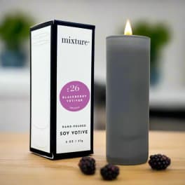 Gray soy votive candle beside its box with blackberries on a table