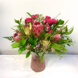 Pink protea and roses arranged in a ribbed glass vase