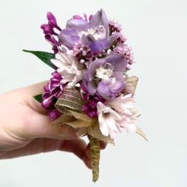 Small handheld boutonniere of purple and pink flowers with a gold ribbon-wrapped stem.