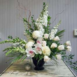 Tall white floral arrangement in a black vase with orchids and roses