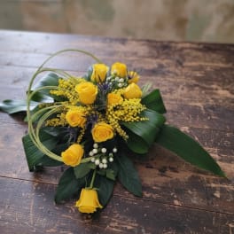 Low arrangement of yellow roses with white berries and looped grass on a wooden table