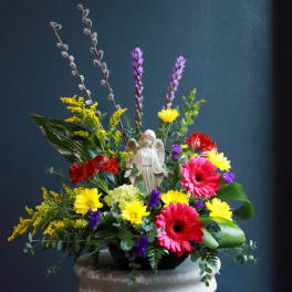 Colorful floral arrangement with an angel figurine in a low black bowl