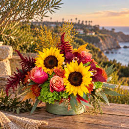 Sunflower and rose arrangement in a green container on a wooden table