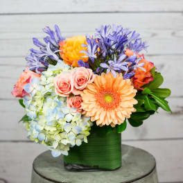 Colorful bouquet in a green wrapped container with roses, hydrangeas, and daisies