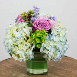Pink roses and blue hydrangeas in a green glass vase
