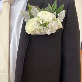 White boutonniere on a dark suit jacket with a cream tie