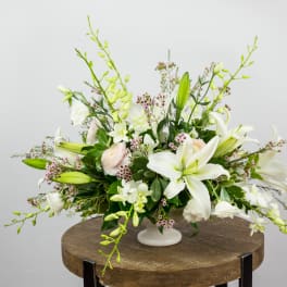 White lily and orchid arrangement in a white pedestal vase