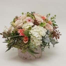 Round bouquet of blush and white flowers in a speckled box.