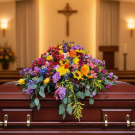 Bright mixed floral casket spray in vivid colors on a polished wood casket