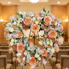 Heart-shaped wreath of peach and cream roses and mixed flowers on a standing easel in a chapel